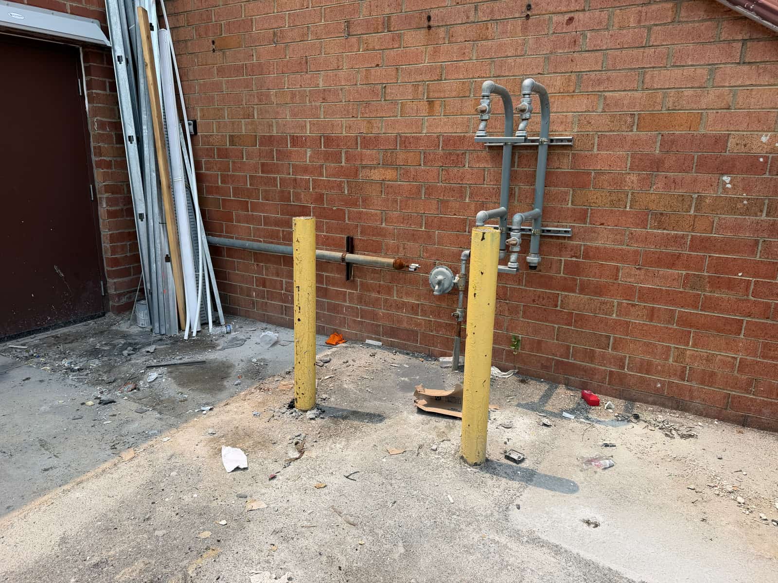 The same corner of the building with the debris pile gone, only the yellow bollards and bare concrete left