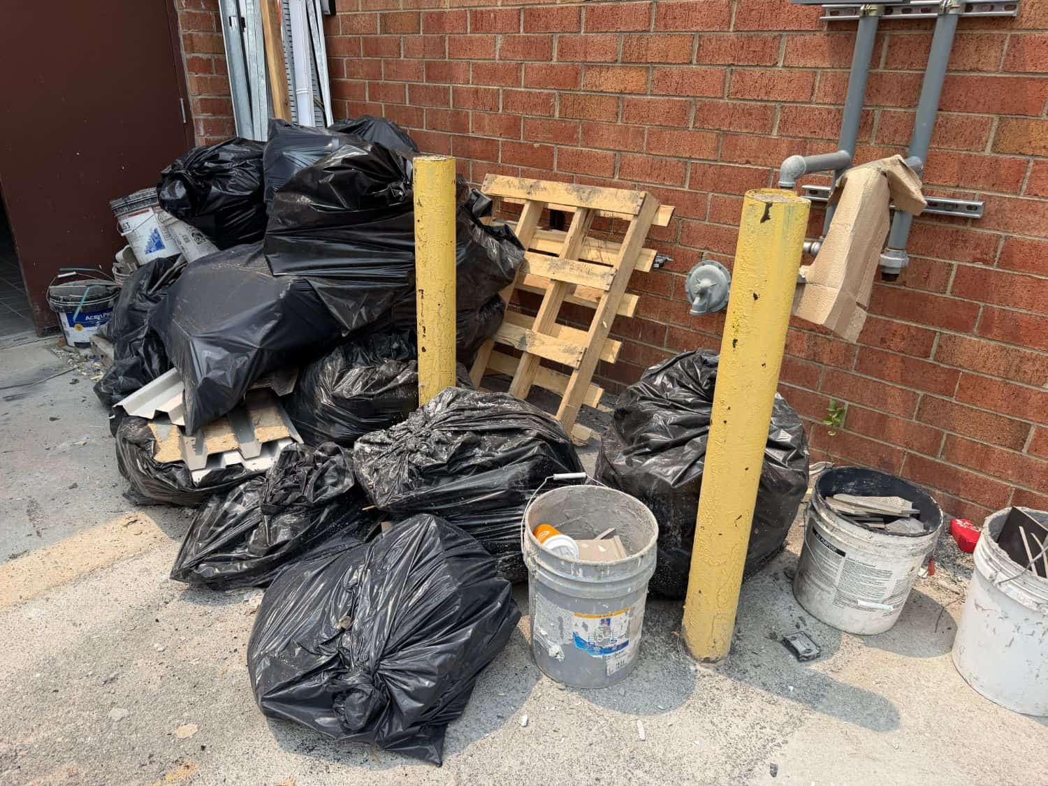 Bagged construction debris, pallets, paint buckets and scrap trim piled against a brick wall at a Delaware commercial site