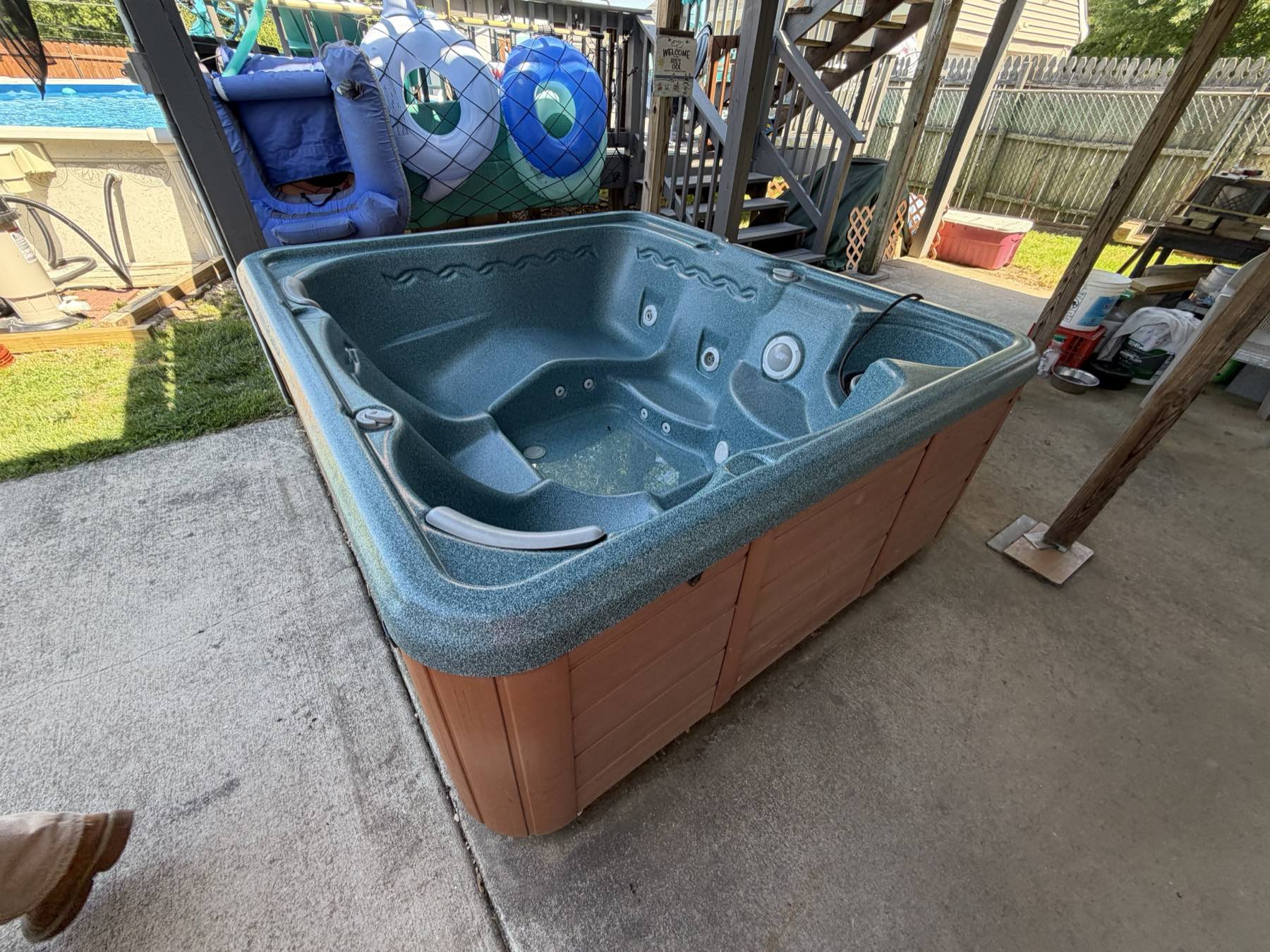 An old teal hot tub with a wood surround sitting on a Delaware backyard patio