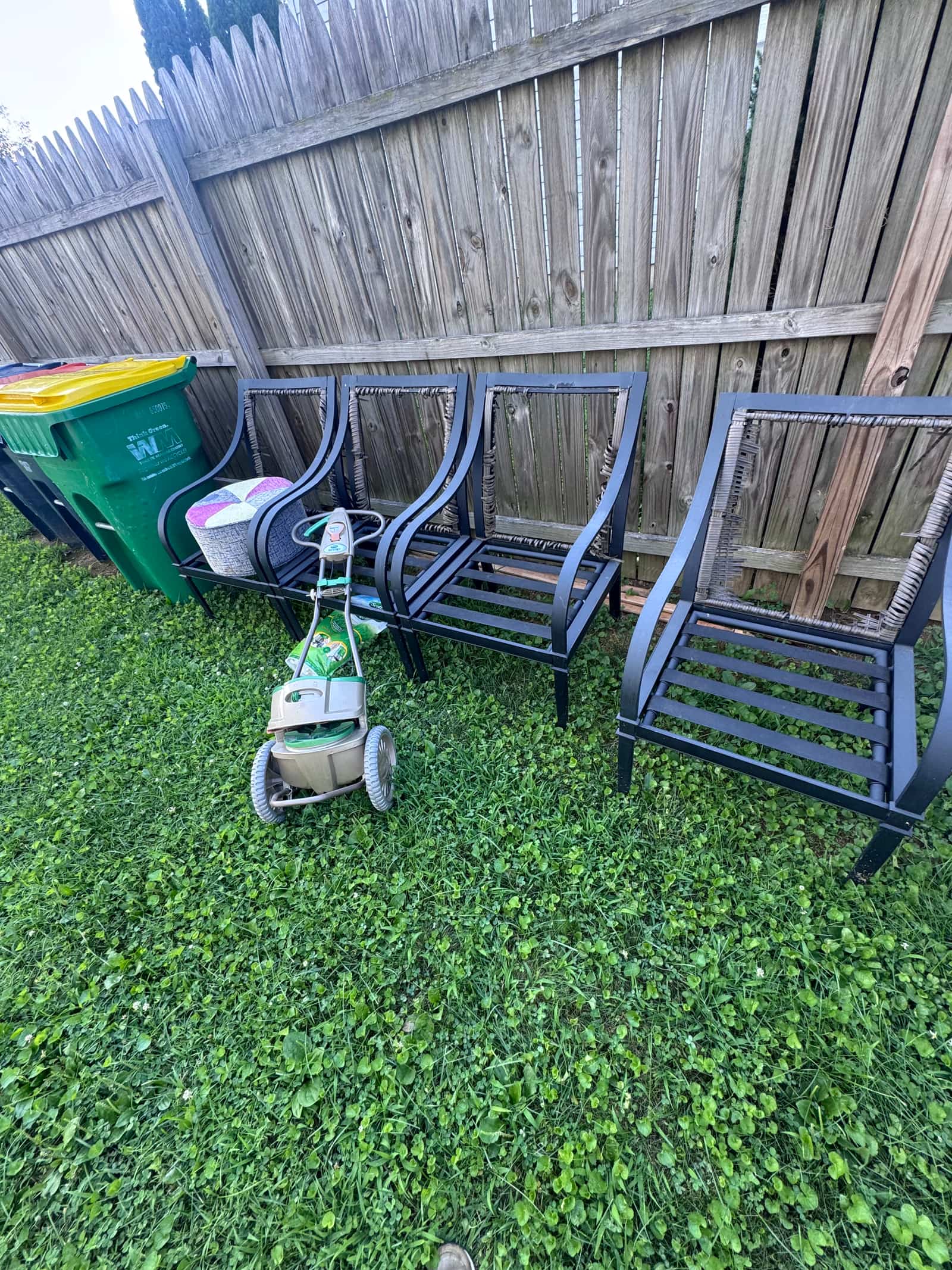 Metal patio chair frames and a lawn spreader against a wood fence in a Middletown, DE backyard before removal