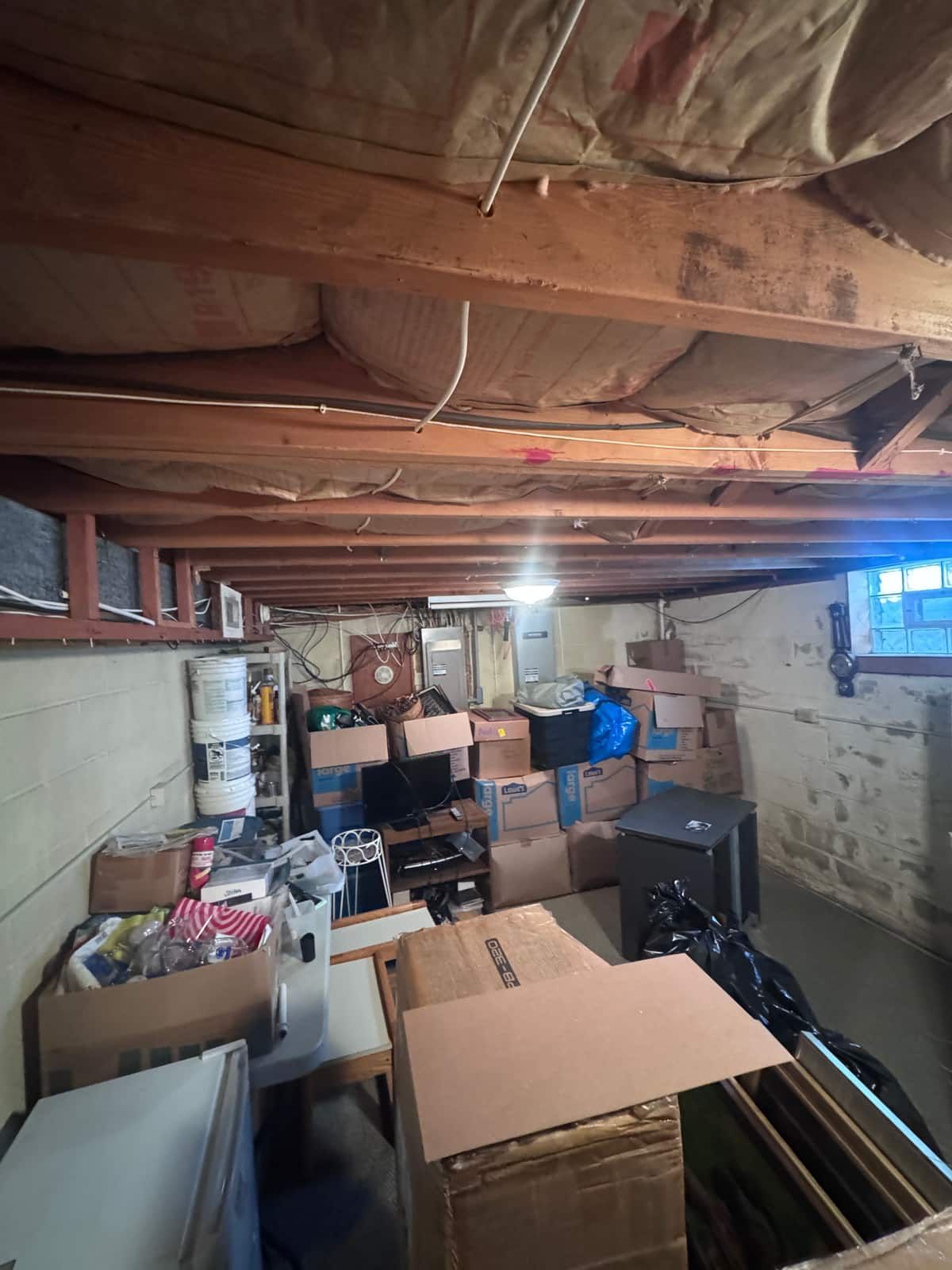 An unfinished Wilmington basement packed with boxes, bins and furniture before the cleanout
