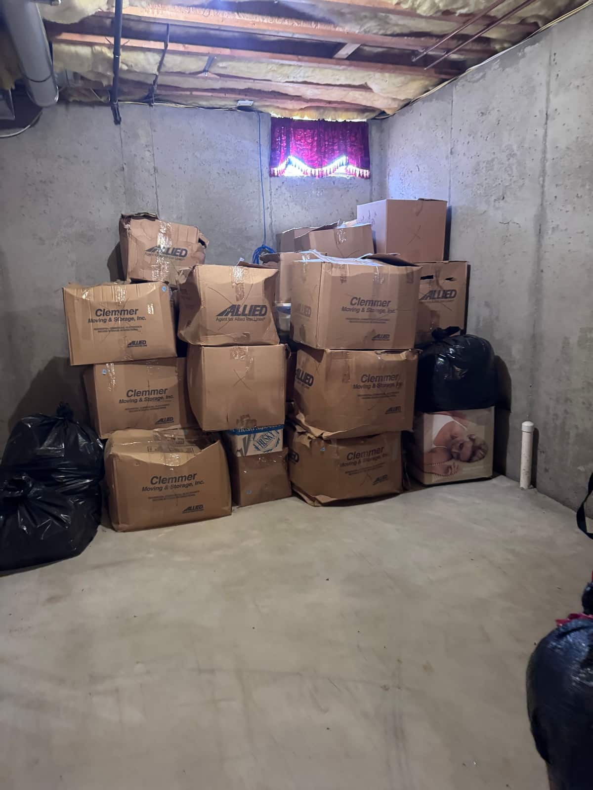 Moving boxes stacked several high against the wall of an unfinished Middletown basement, with trash bags beside them