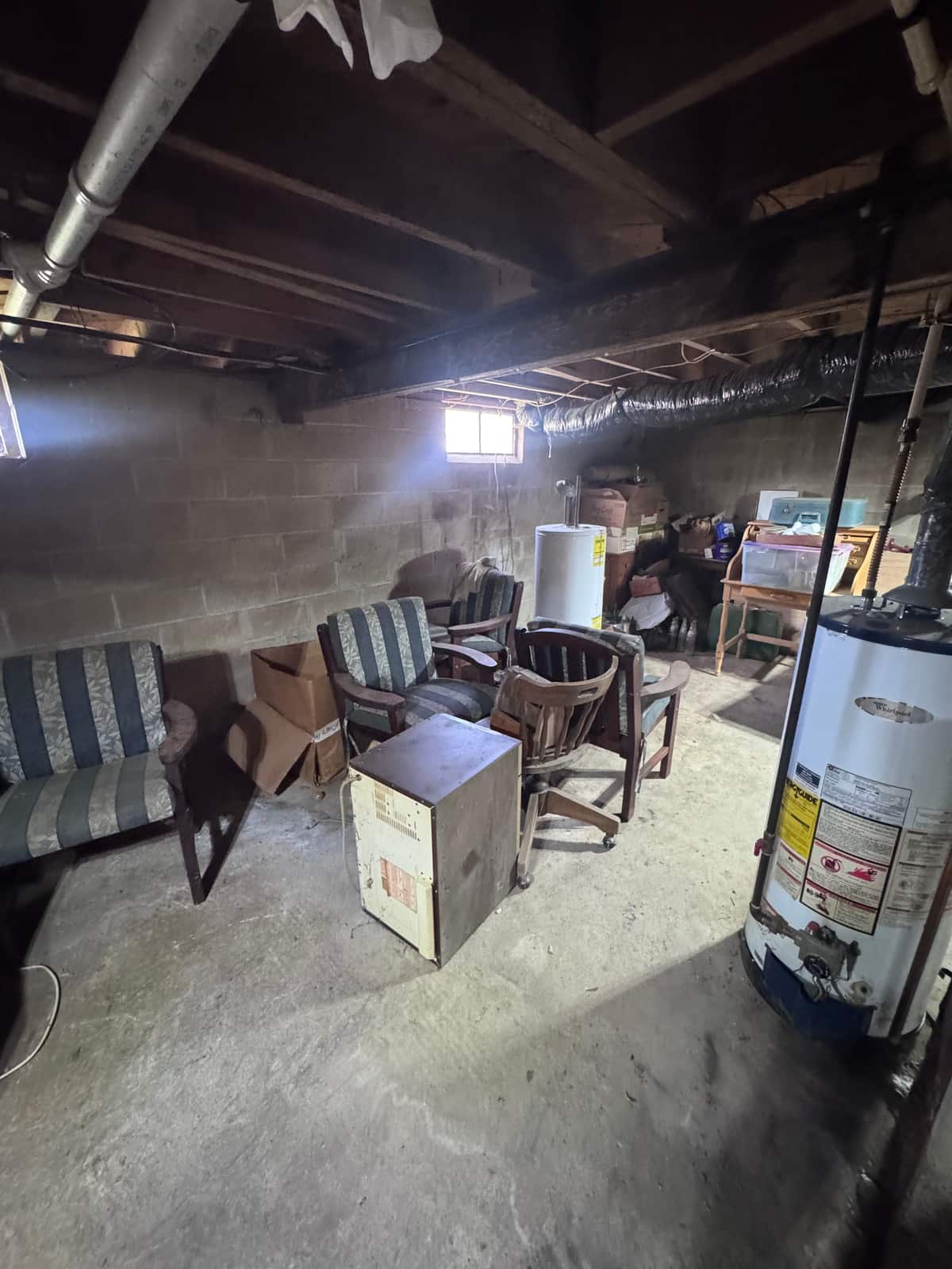 Old chairs, a cabinet and boxes along the wall of an unfinished Smyrna basement before the cleanout