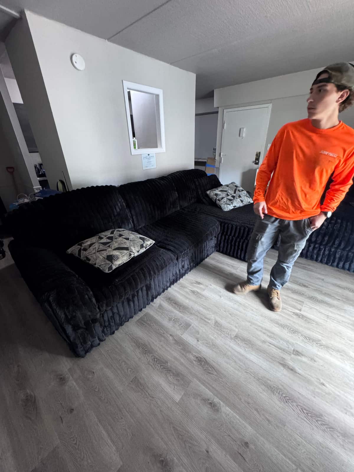 A large black sectional couch in a Wilmington apartment, with a Junk Away crew member in an orange shirt standing beside it before the carry-out