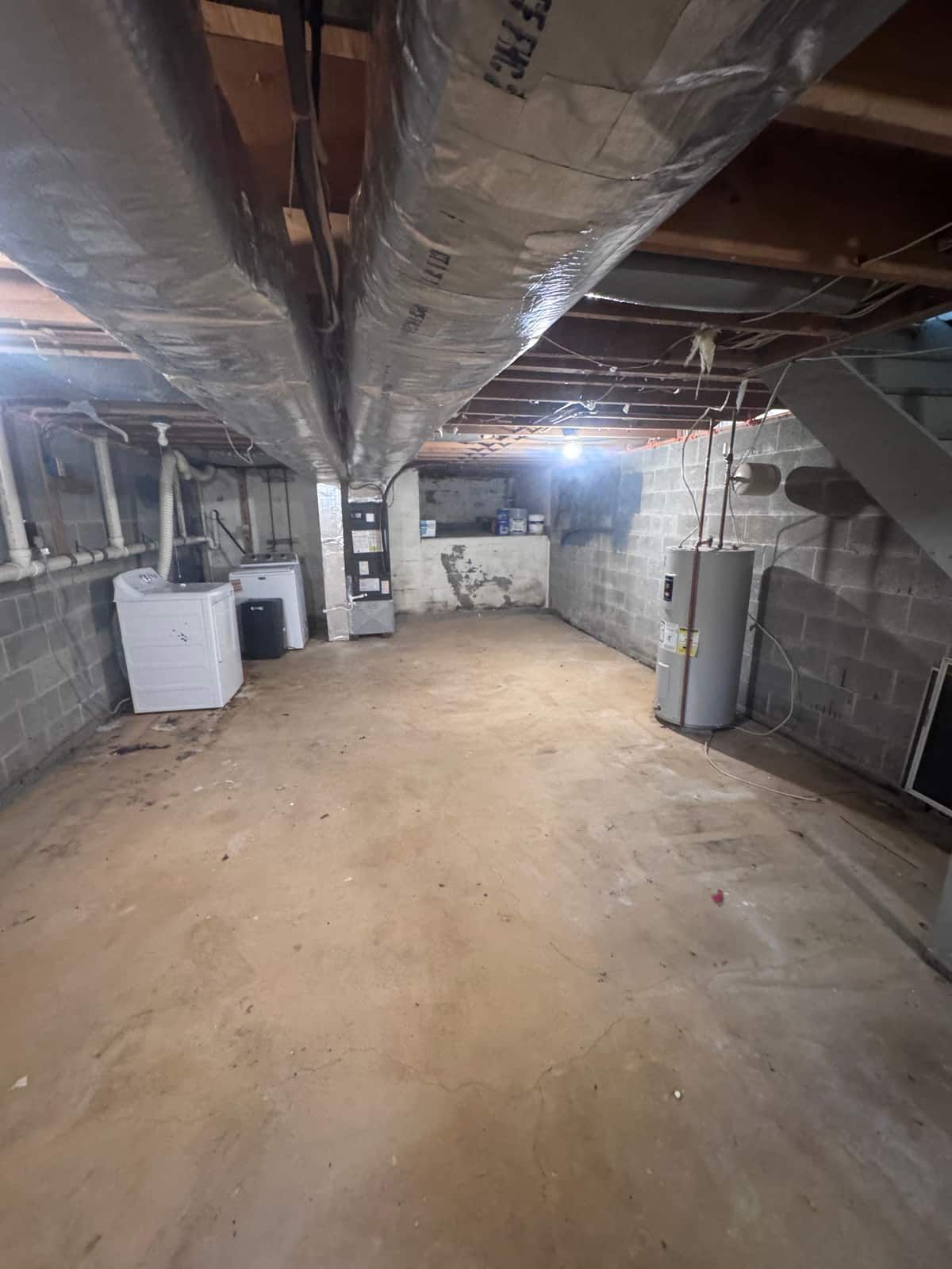 The same basement cleared to the concrete floor, with the washer, dryer and water heater left in place