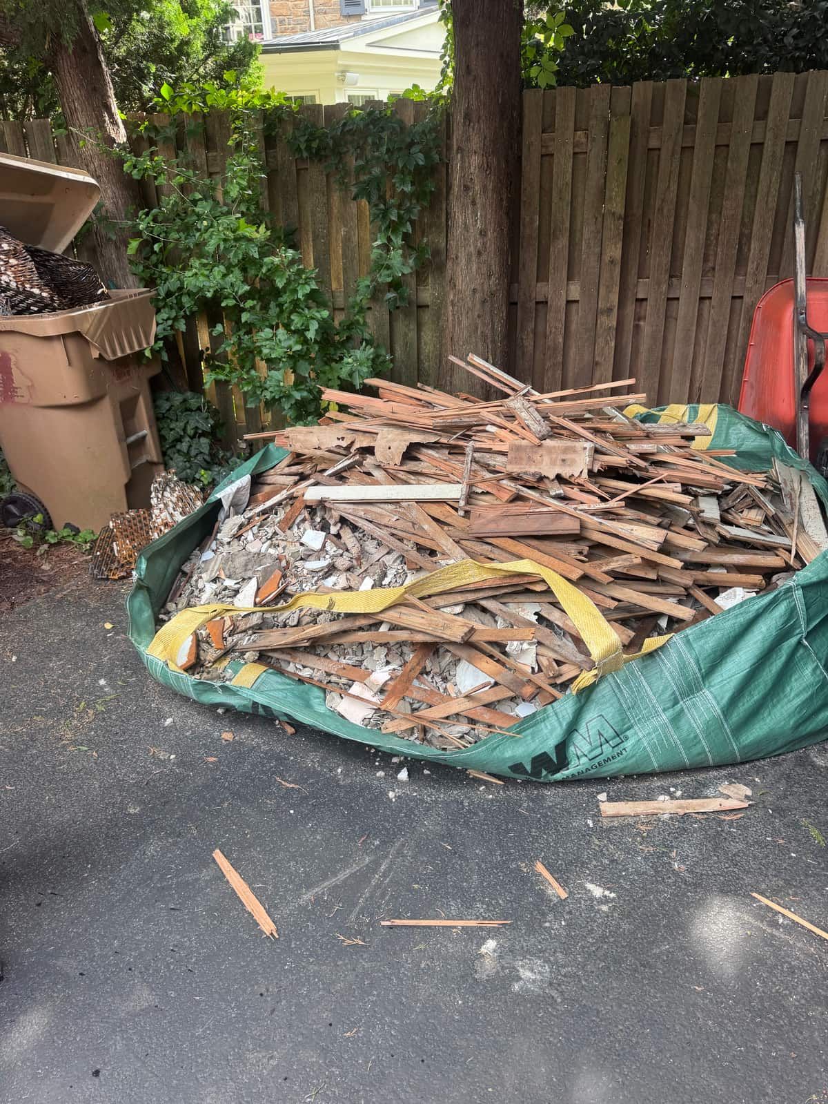 A bulk bag full of bathroom tear-out debris on a narrow Wilmington driveway beside a wooden fence