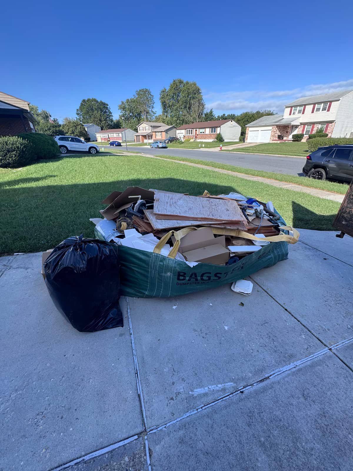 A bulk bag and a black trash bag of demolition material on a Dover driveway before pickup