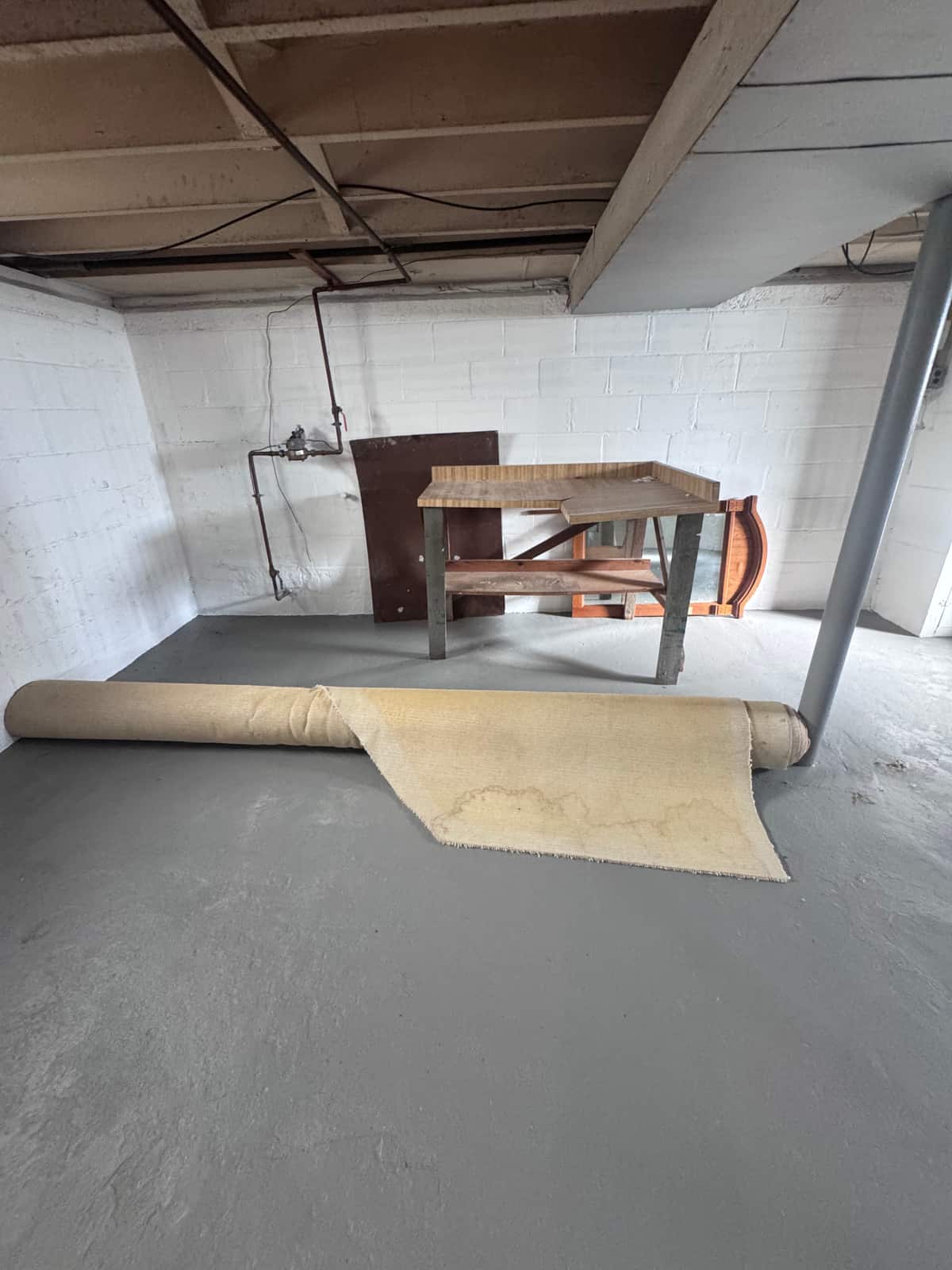 An unfinished Wilmington basement with a rolled carpet, a workbench and a few panels left against the block wall before the cleanout